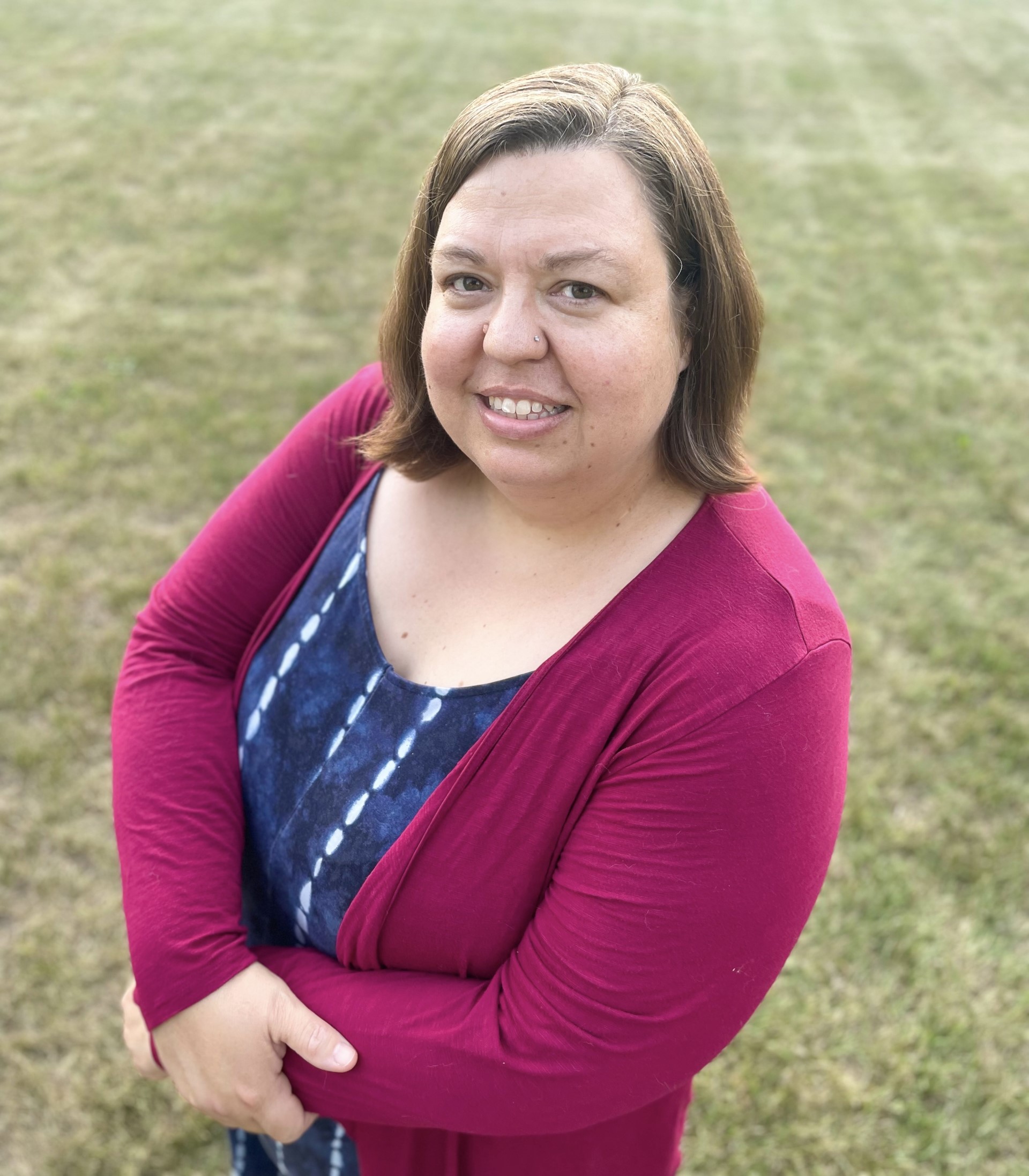 Woman in blue jumper and maroon cardigan standing in the grass.